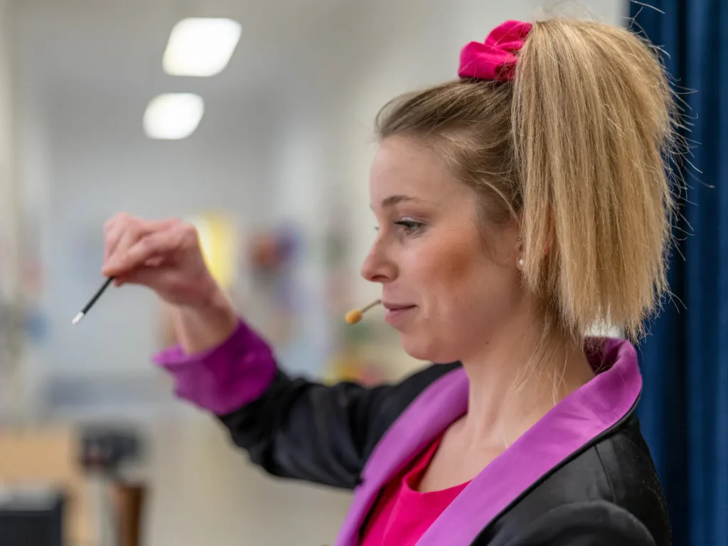 Kinderzauberin Bombastini im pinken Kostüm hält konzentriert den Zauberstab hoch – Nahaufnahme im Seitenprofil