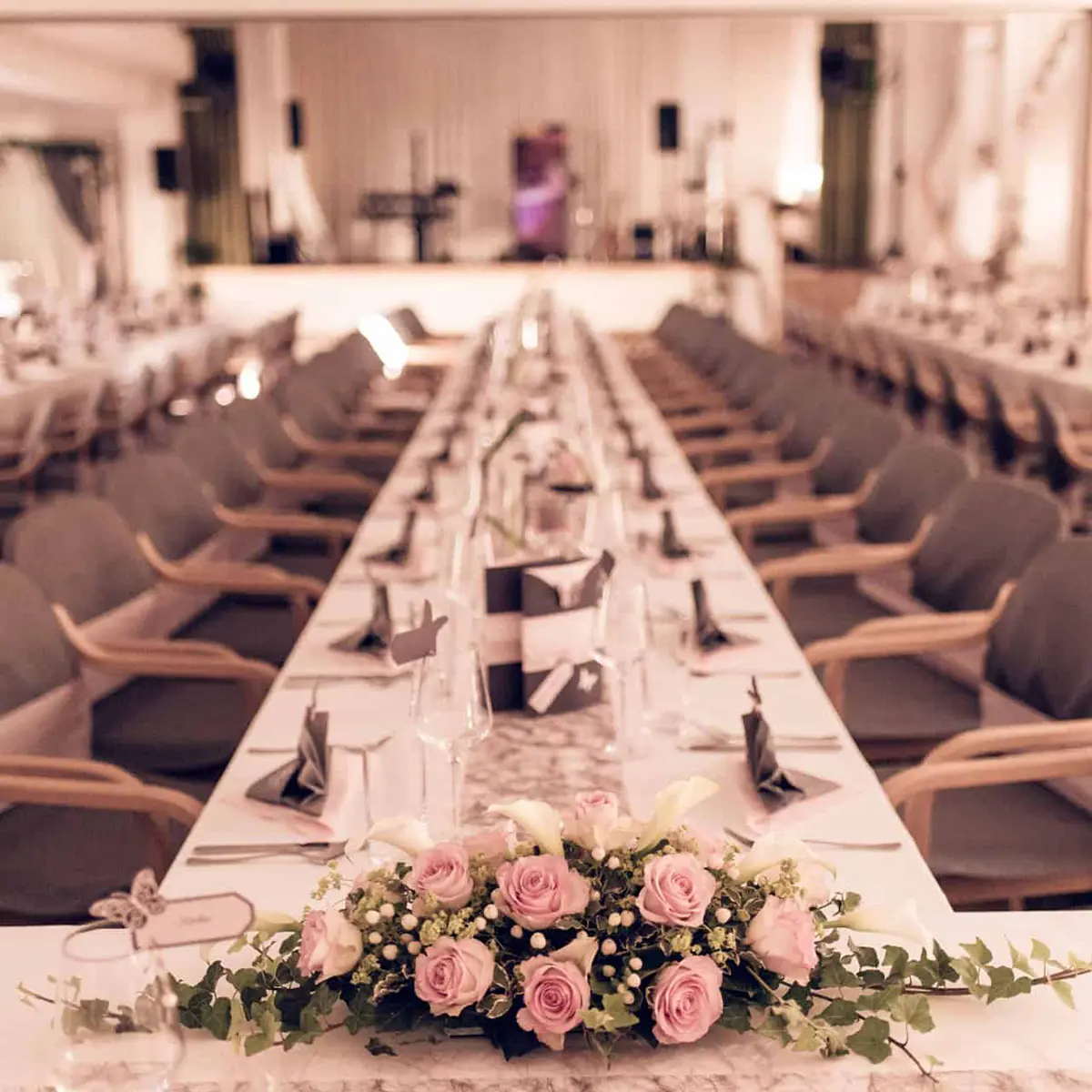 Hochzeitssaal - Ein langer Tisch mit weißen Tischdecken und rosa Blumen dekoriert